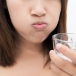 woman rinsing mouth with water after brushing teeth